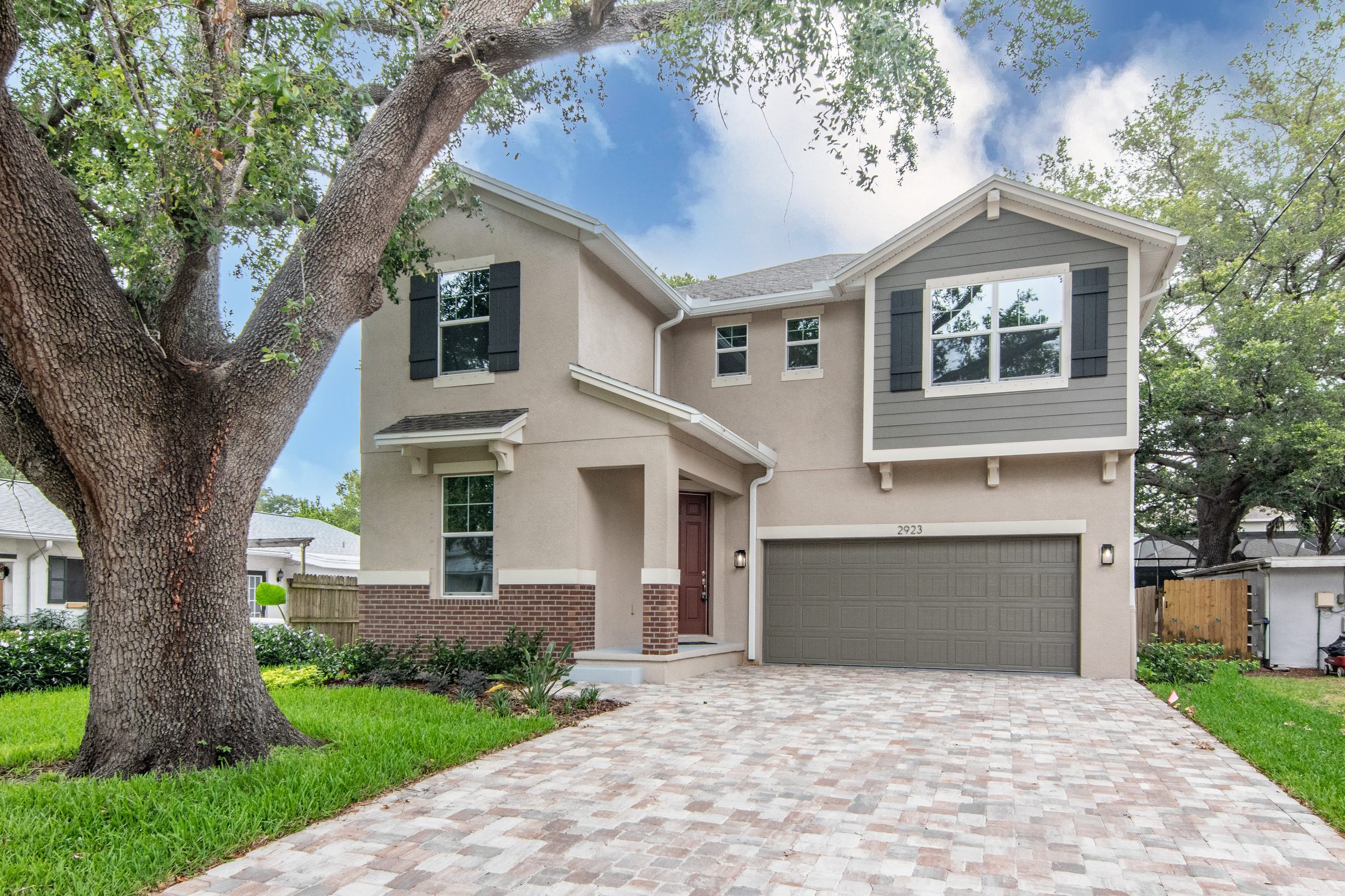 Two-story home with a paver driveway under a live oak