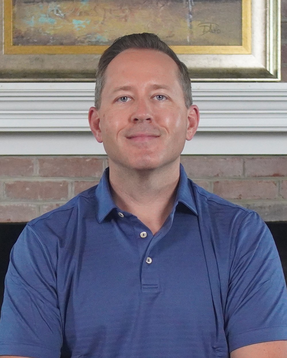 Cody Powell smiling in a blue polo in front of a fireplace